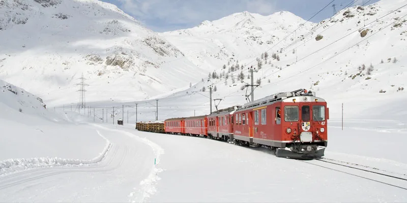 jungfraujoch red train ride in snowy mountainous under cloudy sky.